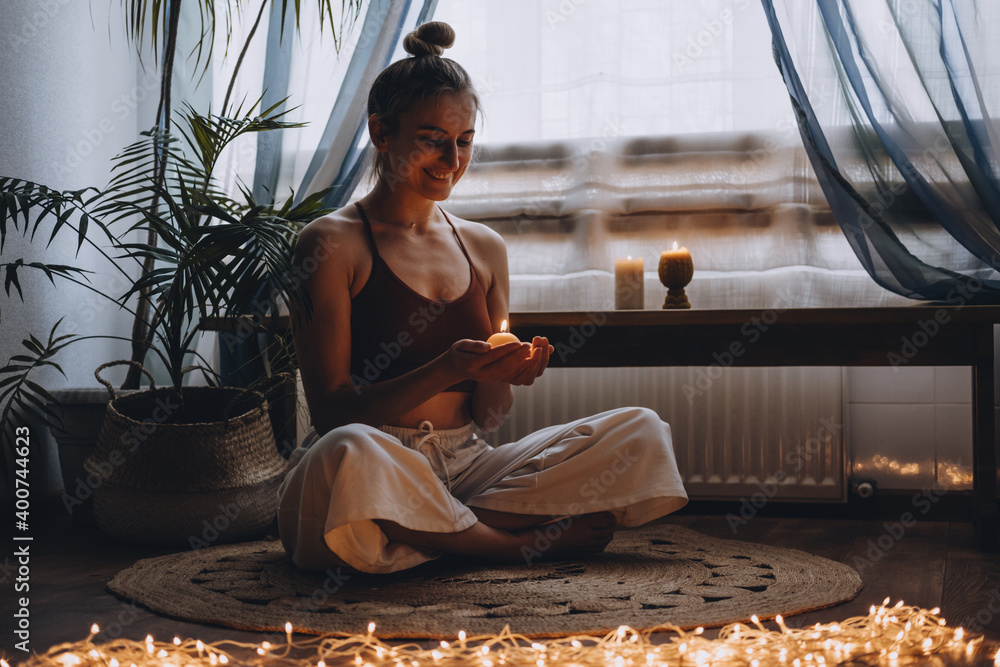 Young woman sitting on the floor, lights candles, enjoy meditation, do yoga exercise at home. Mental health, self care, No stress, healthy habit, mindfulness lifestyle, anxiety relief concept